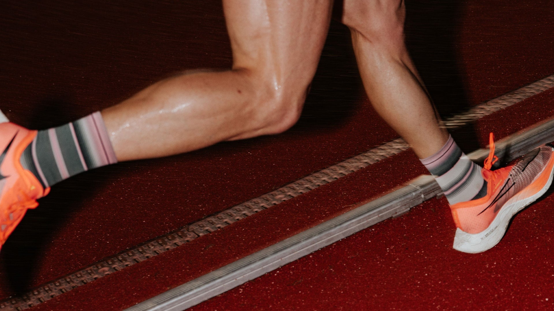 Close-up of a runner's legs in striped socks and bright orange shoes on a track.