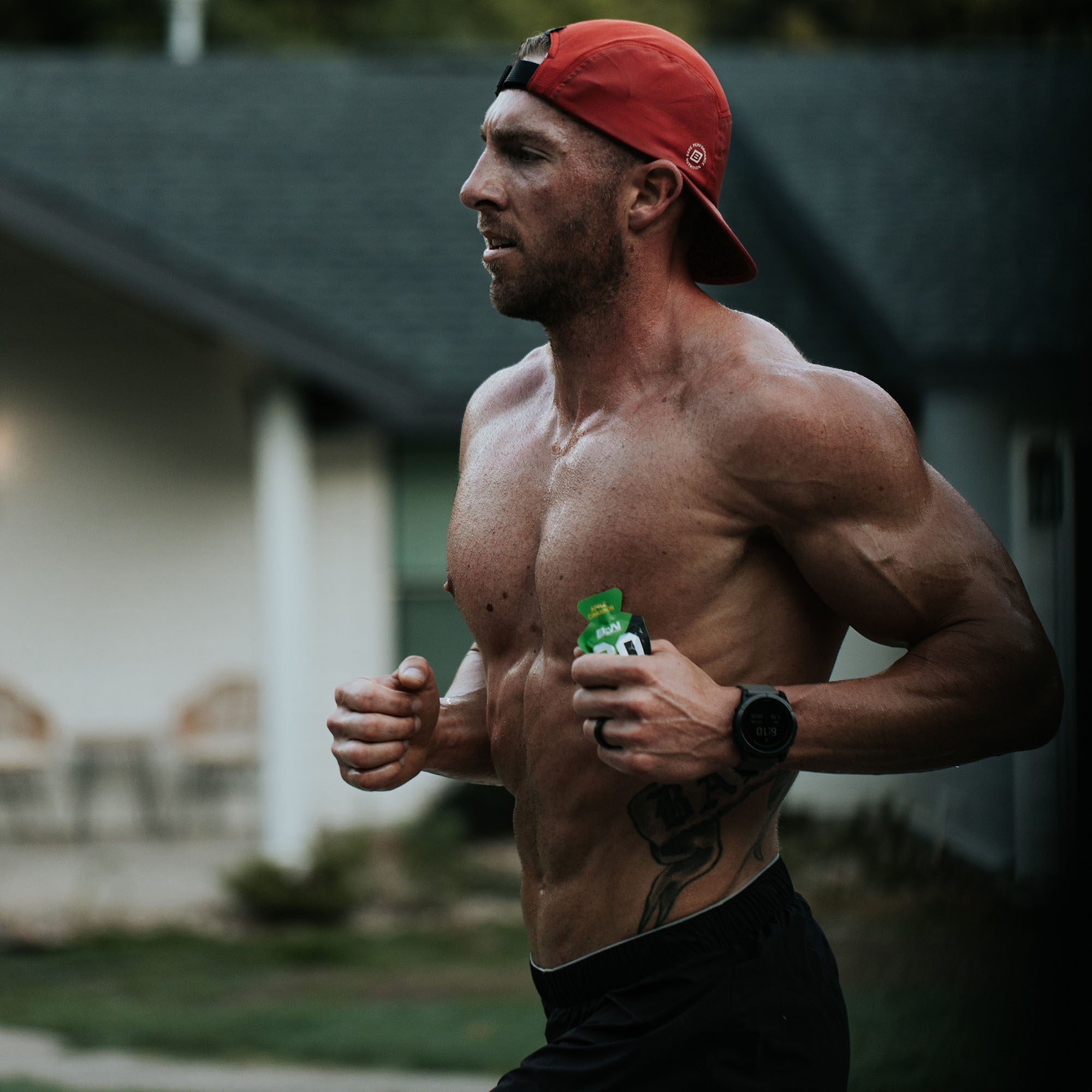 Shirtless man wearing a red cap running outdoors, holding a fitness gel pack.