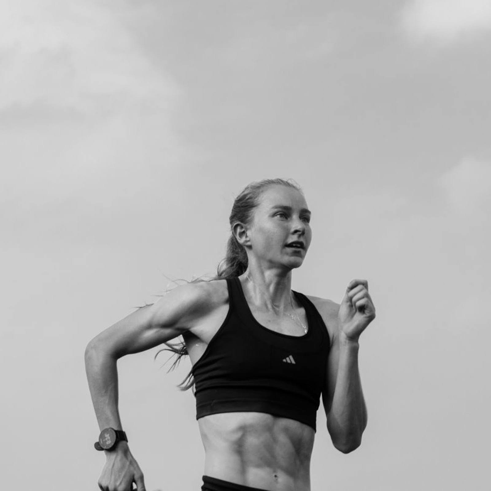 Woman running outdoors, wearing a sports bra and fitness watch.